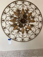 Large round iron wall decor featuring intricate floral design with bronze finish on wall.