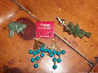 Photo showing 14K gold wire turquoise bead chandelier earrings attached to Longans Originals branded card, jade butterfly brooch, and jade Christmas tree pendant laid on wooden surface.