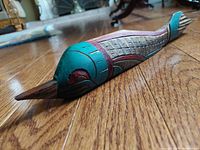 Side view of the carved and painted wooden fish showing detailed scale carving and vibrant colors on hardwood floor.