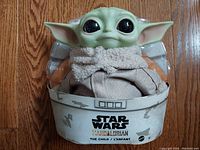 Front view of the packaged figure showing the detailed figure of The Child with large black eyes and tan robe in themed packaging.