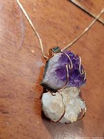 Close-up of custom stone pendant showing rough purple amethyst and rough citrine stones wrapped with gold wire on gold chain.