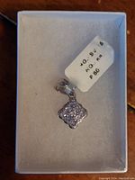 Front view of the silver pendant resting in a white jewelry box showing the tanzanite stones cluster and attached price tag