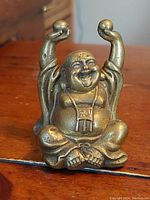 Front view of a small vintage solid cast bronze Buddha statue sitting cross-legged with arms raised holding spheres.