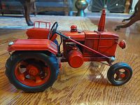 Side view of vintage red metal folk art farm tractor on wooden floor showing left profile