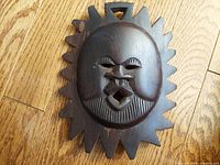 Front view of the carved wood sun mask showing face detail and sunburst pattern.