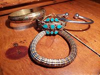 Group of four vintage brass and turquoise bracelets on wooden surface showing all items clearly.