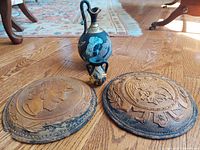 Photo showing two pottery vases and two wooden sculpted art discs arranged on wood floor.