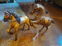 Both horse figurines side by side on hardwood floor showing size and color contrast