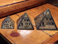 Three metal pyramids of varying sizes with etched Egyptian hieroglyphics and Sphinx design on a wooden surface