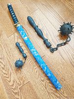 Photo showing Oriental samurai sword with blue and gold dragon decorated scabbard next to two European ball and chain items with wooden handles of different sizes.