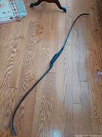 Full view of the vintage PSE recurve bow placed on a wooden floor, showing the full length and the gentle curve of limbs.
