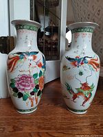 Pair of tall Oriental vases with dragon and phoenix motifs, raised floral decor, standing on wooden floor with door hinge in background