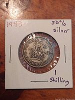 Photo of the coin in card holder showing reverse with lion on crown and inscriptions, dated 1943.