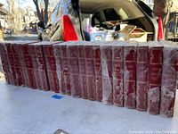 Row of 22 burgundy leather-bound books in plastic sleeves on table
