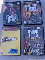Four PlayStation 2 game cases: Guitar Hero, Guitar Hero II Legends of Rock, Guitar Hero Aerosmith, Crazy Taxi Greatest Hits. Price tags visible on the cases.