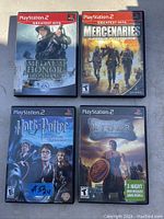 Photo of four PlayStation 2 game cases: Medal of Honor Frontline, Mercenaries Playground of Destruction, Harry Potter and the Prisoner of Azkaban, Rygar The Legendary Adventure, arranged on pavement with shadow.
