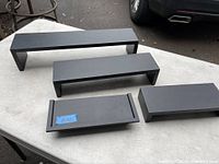 Top view of all four black rectangular wall shelves displayed on a table outdoors.
