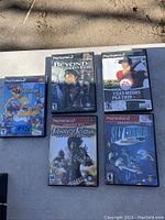 Photo showing five PlayStation 2 game cases arranged on a surface, each game visible with cover art.