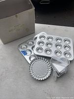 Photo showing multiple aluminum bakeware pans and molds with the original box at the background.