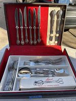 Full set of vintage stainless steel cutlery in red velvet lined case, showing knives, serving forks, forks, spoons, and other utensils.