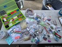 Overview of arts and crafts lot with beads, rubber bands, and tools on a table, showing plastic bags and various supplies.