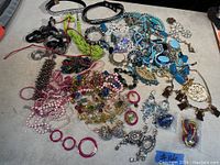 Top view of assorted costume jewelry laid out on a table including colorful bead necklaces, earrings, bracelets, and pendants in various styles and colors.