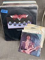 Photo showing a stack of LP vinyl records with Aerosmith's album "Rocks" on top, along with a small collection of 45rpm singles including one featuring a musician playing guitar.