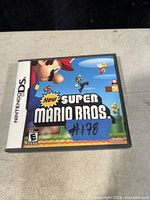 Front view of the New Super Mario Bros. game case for Nintendo DS showing the cover art and a blue tape with '#178' written on it.