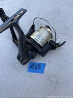 Side view of Shimano 2000 spinning fishing reel showing spool and handle assembly, with a blue tag #67.
