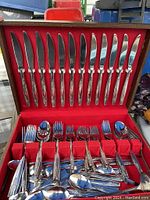 Full view of knives, forks, and spoons arranged in red velvet-lined cutlery box.