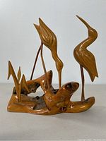 Front view of wooden sculpture showing two large herons and two small birds on natural wood base