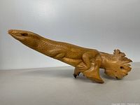 Side view of the wooden lizard figurine showing detailed scaly texture and wood grain with the tail resembling a natural root formation.