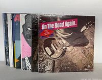 Twelve sealed vinyl records stacked, showing various album cover art including "On The Road Again".