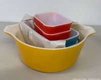 Yellow Pyrex mixing bowl with four nested refrigerator dishes in red, pink, turquoise, and light blue