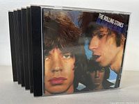 Eight jewel case CDs stacked showing front album cover 'Between the Buttons' by The Rolling Stones.