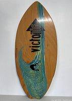Full view of wooden Victoria skimboard showing painted wave design and branded logo.