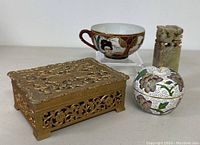 All four items displayed together showing the brass jewelry box, teacup, cloisonné apple trinket box, and soapstone chop seal.