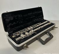 Open black hard case showing the vintage Bundy flute disassembled in three parts inside black plush interior.