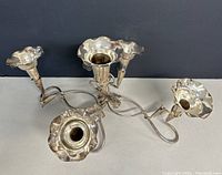 Front and angled view of the silver plated Art Nouveau epergne showing five flower trumpet holders with curling stems and leaf details on a dark background.