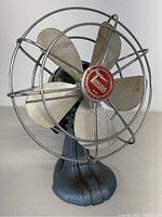 Front view of vintage Torcan electric fan showing metal blades, protective cage, and blue claw-foot base.