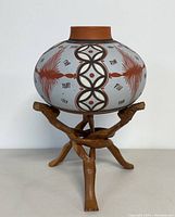 Front view of ceramic vase on wooden tripod stand showing geometric patterns and stand design.