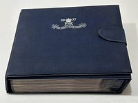 Closed dark blue binder with silver embossed Queen's Silver Jubilee emblem and clasp visible on the side.