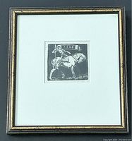 Full view of framed black and white block print showing the image centered with matte and black and gold frame.