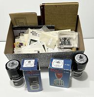 Photo showing large cardboard box filled with stamp stock books, envelopes, ephemera and 2 Colop printer stamps with original boxes in front.
