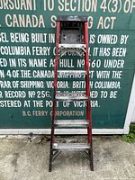 Front view of the 6-foot electrician's ladder showing metal steps, red frame, and signs of age with background text about Canada Shipping Act.