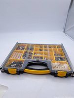 Front view of Stanley plastic carry case with clear lid showing multiple compartments filled with assorted metal and plastic hardware items including screws, bolts, washers, and anchors.