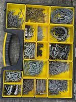 Open Stanley yellow plastic organizer showing various compartments filled with assorted screws, nails, coils of metal wire, bolts, hooks and other hardware.
