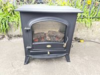 Front view of the black vintage electric faux fireplace heater showing the metal body and glass door with simulated logs inside.