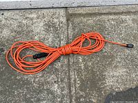 Full length image of the orange extension cable coiled, showing the connectors at each end and overall cable condition on concrete surface.