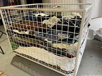 Large white wire mesh basket full of folded assorted vintage clothing items in varied colors and fabrics.